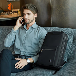 Black backpack with front zip pocket and logo badge, laid on couch