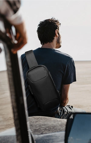 Black crossbody sling bag worn on back with compact front pocket and adjustable strap