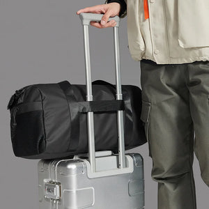 Waterproof duffel bag in black with strap, used over a rolling suitcase handle