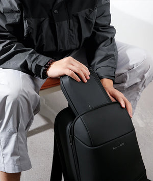 Black crossbody tech bag with front zip pocket, held in hand