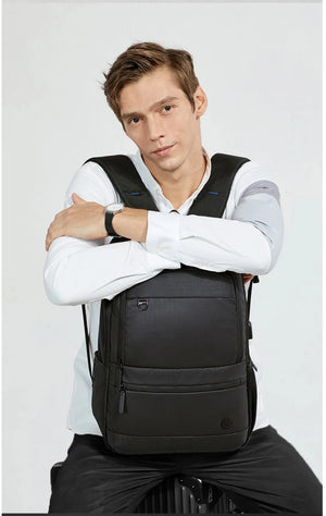 Black travel backpack worn by man, with front zipper pocket and adjustable straps