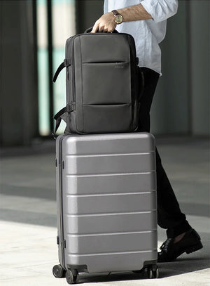 Waterproof travel backpack secured over a rolling suitcase with a top trolley strap