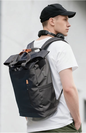 Black roll-top waterproof backpack worn from the side with orange zipper pull and cap.