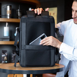 Black backpack on table with front grab handle, side straps, and phone connected charging