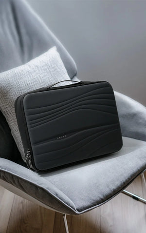 Black padded laptop sleeve with quilted wave pattern, resting on upholstered chair.
