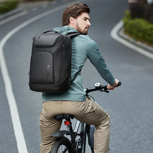 Black waterproof travel backpack worn while riding a bicycle, front pocket and shoulder straps