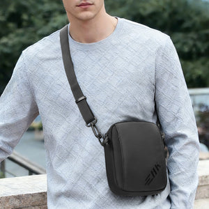 Black small crossbody bag worn with adjustable strap and metal chain-style hardware