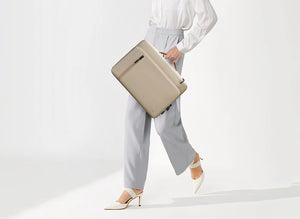 Beige laptop bag carried by hand with top handle and zip closure