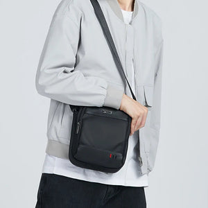 Black compact messenger bag worn crossbody with front logo plate detail