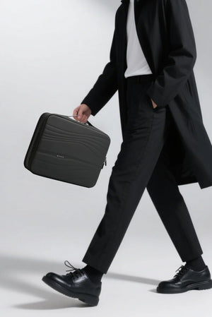 Black padded laptop sleeve carried by person, front zip pocket and handle visible.