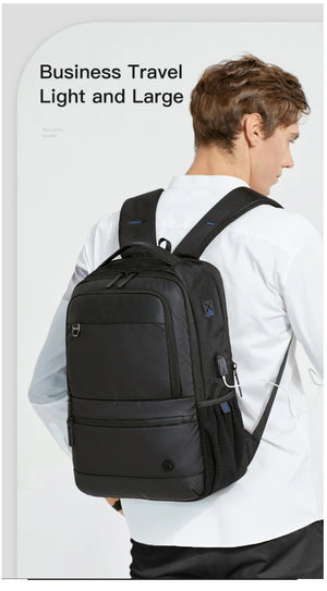 Black travel backpack worn by person, with front zipper pocket and top carry handle
