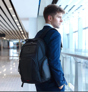 Black waterproof travel backpack worn by a man, with top handle and front pockets