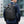 Black roll-top waterproof backpack worn on a person, with orange zipper pull and front pocket.