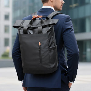 Black roll-top waterproof backpack worn on a person, with orange zipper pull and front pocket.