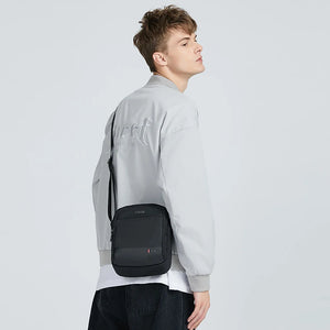Black compact waterproof messenger bag worn crossbody with adjustable shoulder strap
