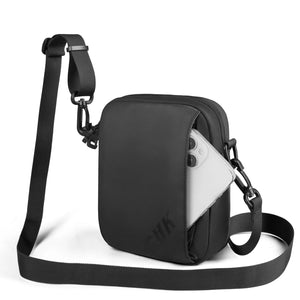 Black crossbody bag with side panel, buckled strap attachments, and front zipper pocket