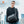 Black crossbody bag worn over hoodie, with front flap and strap buckles
