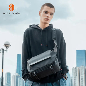 Black crossbody bag worn over hoodie, with front flap and strap buckles