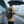 Black travel backpack worn outdoors under an umbrella, with top handle and side buckles visible