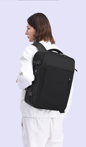 Black travel backpack on a person from side view with front zip pocket and shoulder strap