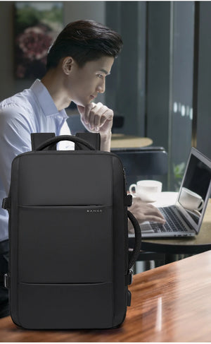Black travel backpack worn by person beside laptop in an office setting