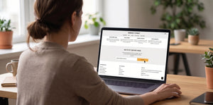 A woman sits at a wooden desk in a bright room, viewed from behind, using a laptop computer. The screen of the laptop displays a subscription box.